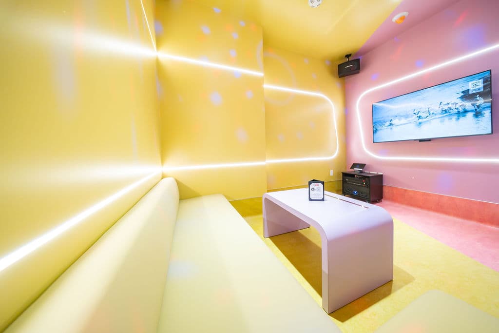 Long yellow sofa facing a screen on a pink wall