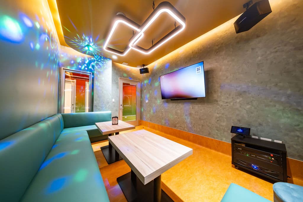 Large karaoke room with a teal booth, wood tables, and a wall-mounted screen
