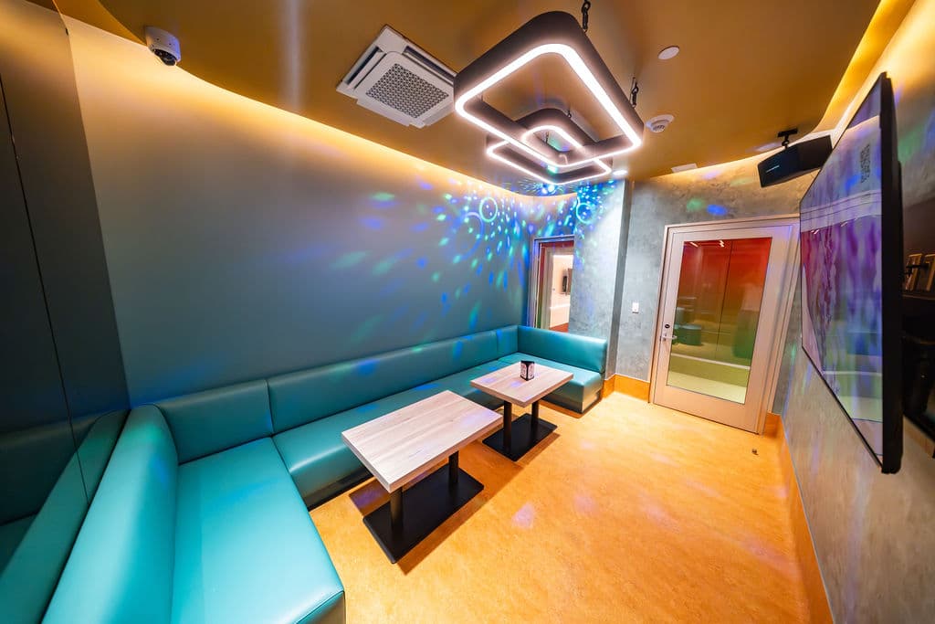 Large karaoke room with a wraparound teal booth under a glowing ceiling light