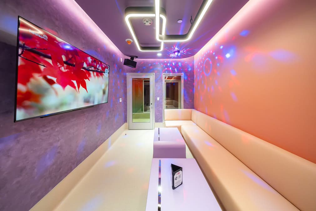 Large karaoke room with a long cream sofa facing a wall-mounted screen