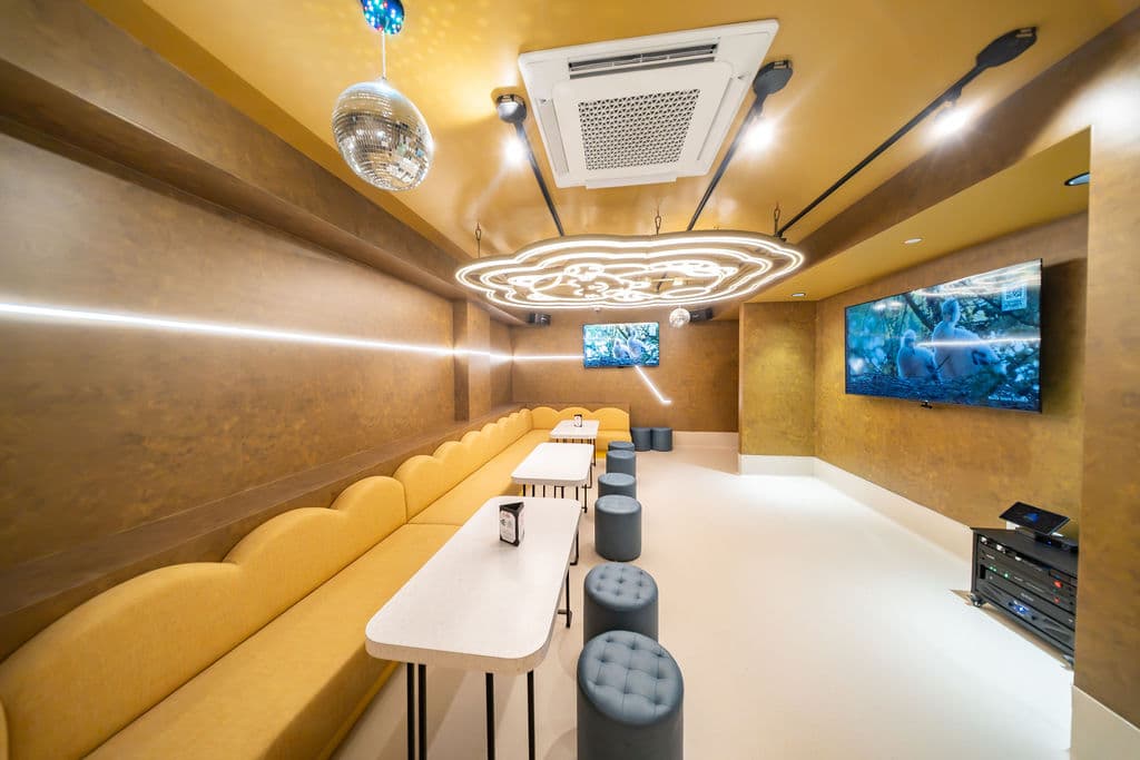 VIP karaoke room with a long scalloped yellow banquette, high tables, and a disco ball