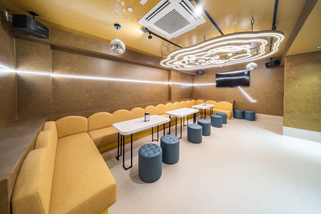 VIP karaoke room with a yellow corner banquette and tables under the glowing Manecky ceiling light