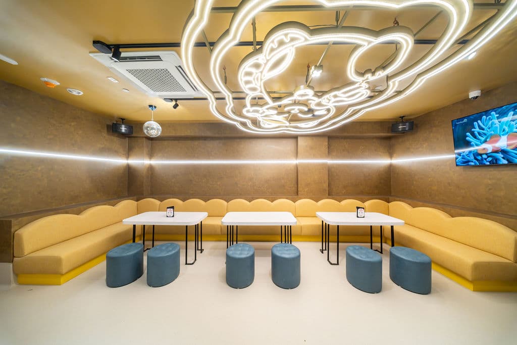 VIP karaoke room with three tables and teal stools facing a wraparound yellow banquette