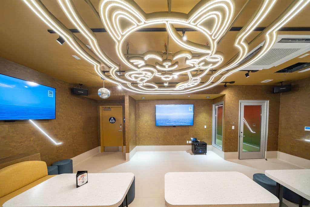 Group karaoke room with two wall-mounted screens under a glowing Manecky ceiling light